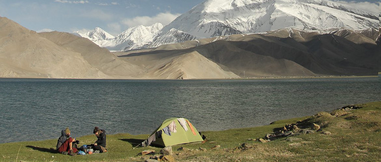 WEIT. DIE GESCHICHTE VON EINEM WEG UM DIE WELT, Zelt an einem See, zwei Menschen campen, im Hintergrund Berglandschaft
