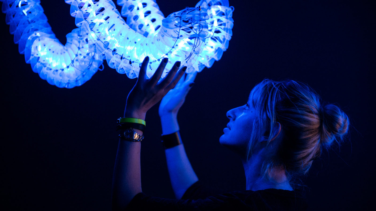 Eine Frau wird von blauen Licht angestrahlt, während sie mit ihren Händen ein Ausstellungsstück berührt.