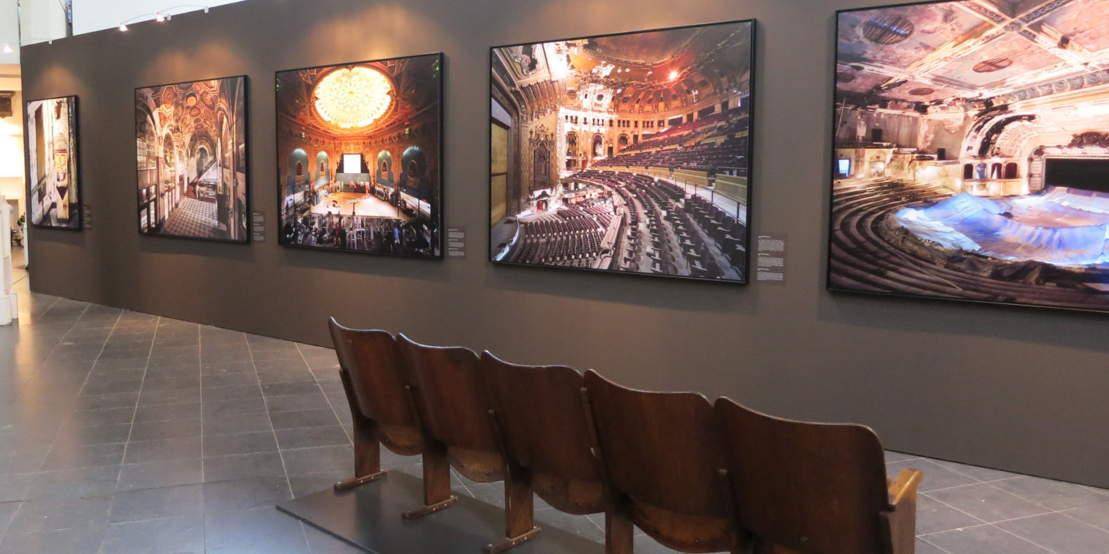 Ausstellungsansicht: Eine Reihe Kinosessel vor einer Wand mit gerahmten Fotografien
