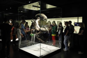 In der Dauerausstellung stehen Besucher:innen um die Vitrine mit dem Alien-Kostüm herum.