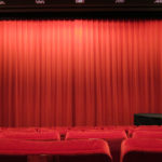 Der rote Vorhang im Kino des DFF ist schwach Beleuchter und einige rote Samtsessel sind zu sehen.