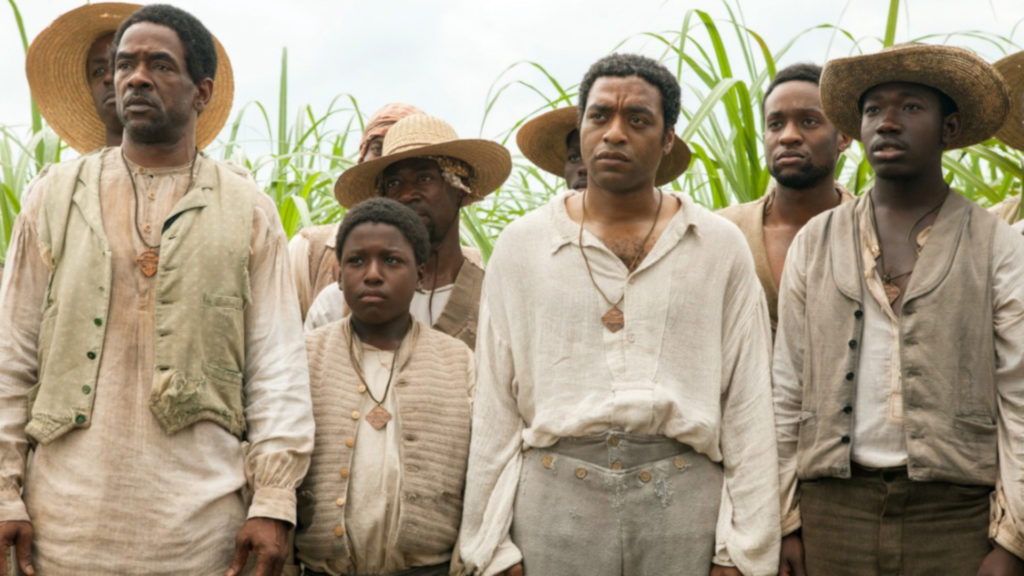 Filmstill Twelve Years a Slave, Acht Darsteller stehen traurig schauend vor einem Feld