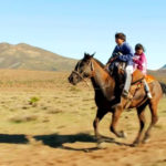 Kinder reiten zu zweit auf einem Pferd durch die Steppe