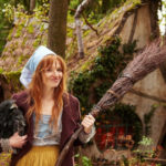 Filmstill Karoline Herfurt als die kleine Hexe vor ihrem windschiefen Haus im Wald mit Besen in der Hand