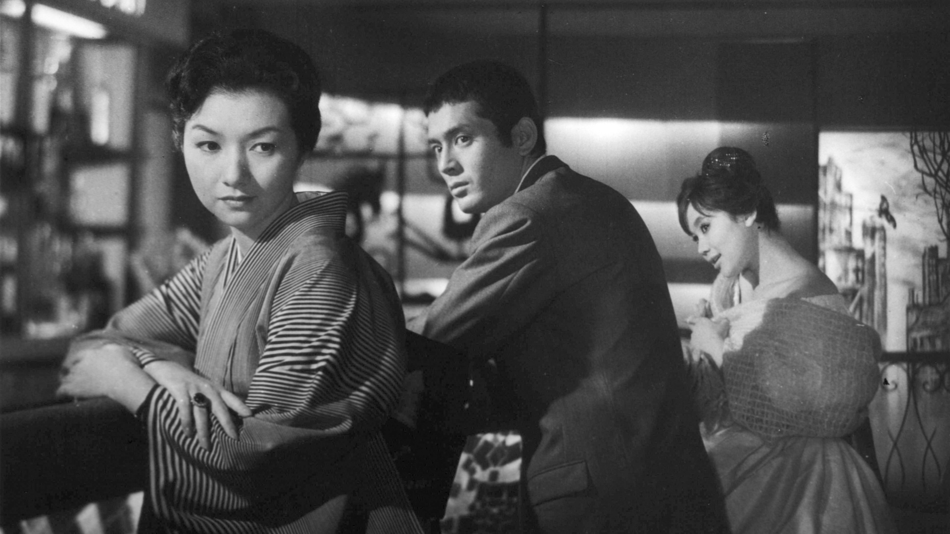 Filmstill aus dem Schwarz-Weiß-Film Nippon. Ein Mann schaut eine Frau an, die sich aber von ihm wegdreht. Eine weitere Frau sitzt im Hintergrund.