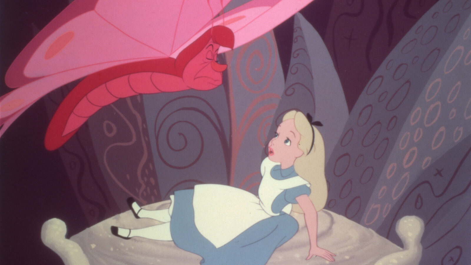 Filmstill aus Alice im Wunderland. Alice sitzt auf einem Kissen und schaut einen roten Schmetterling an.