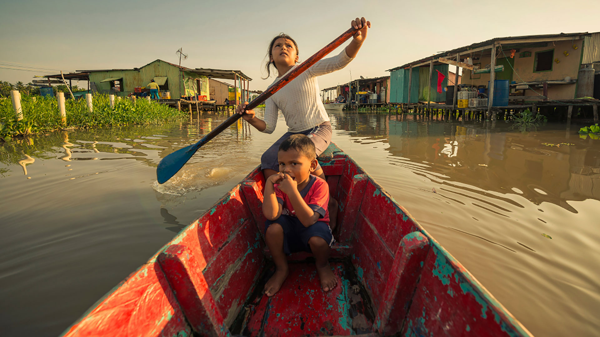 Filmstill aus Once upon a Time in Venezuela. Ein Mädchen sitzt in einem bunten Holzboot mit einem weiteren Kind und paddelt.