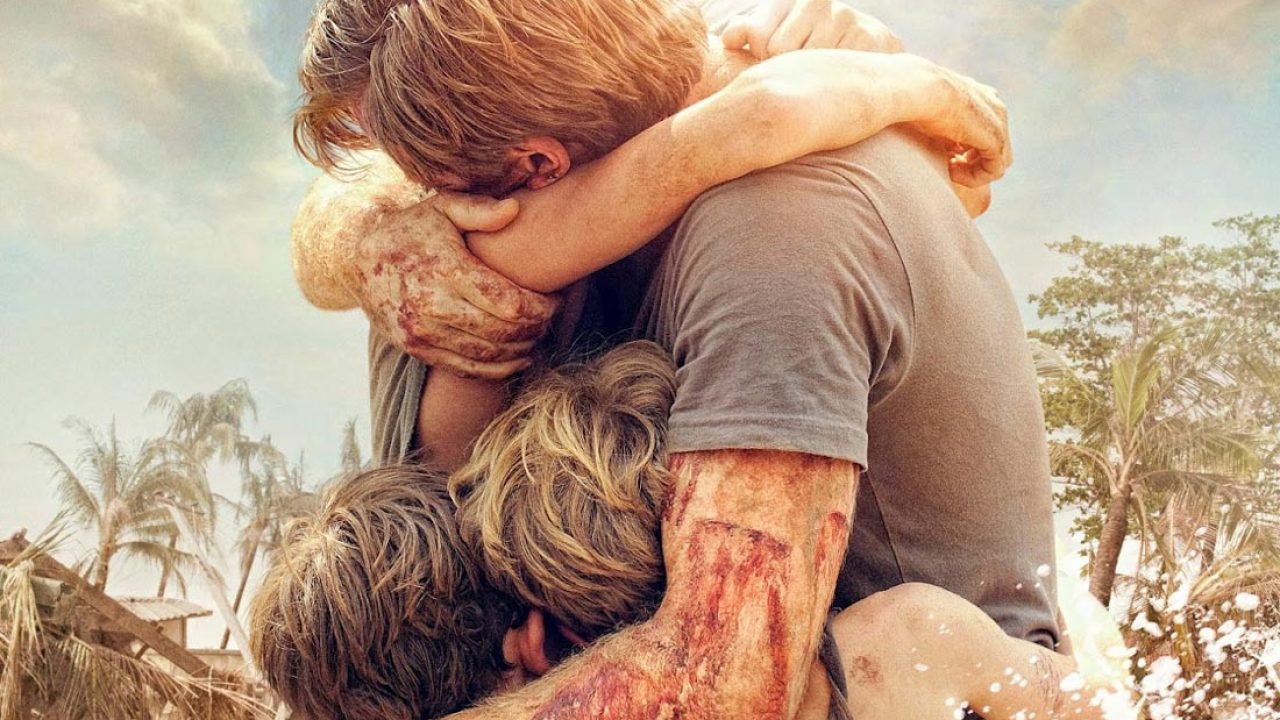 Filmstill aus The Impossible. Ein Mann umarmt mehrere Personen gleichzeitig. Seine Arme und Hände sind mit Blut und Dreck beschmiert.