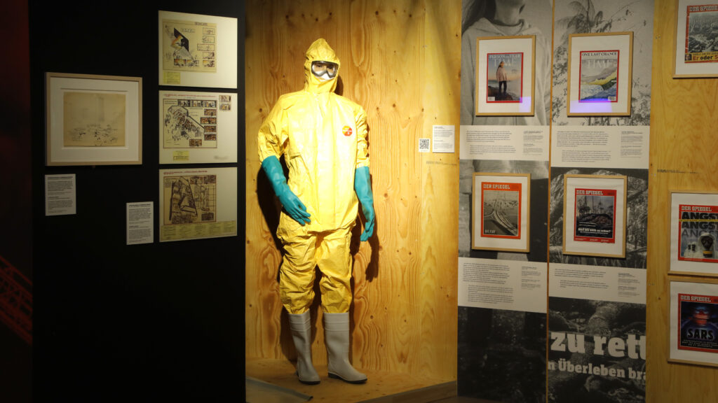 Gelber Anzug zum Schutz vor chemikalien mit blauen Handschuhen in der Ausstellung KATASTROPHE