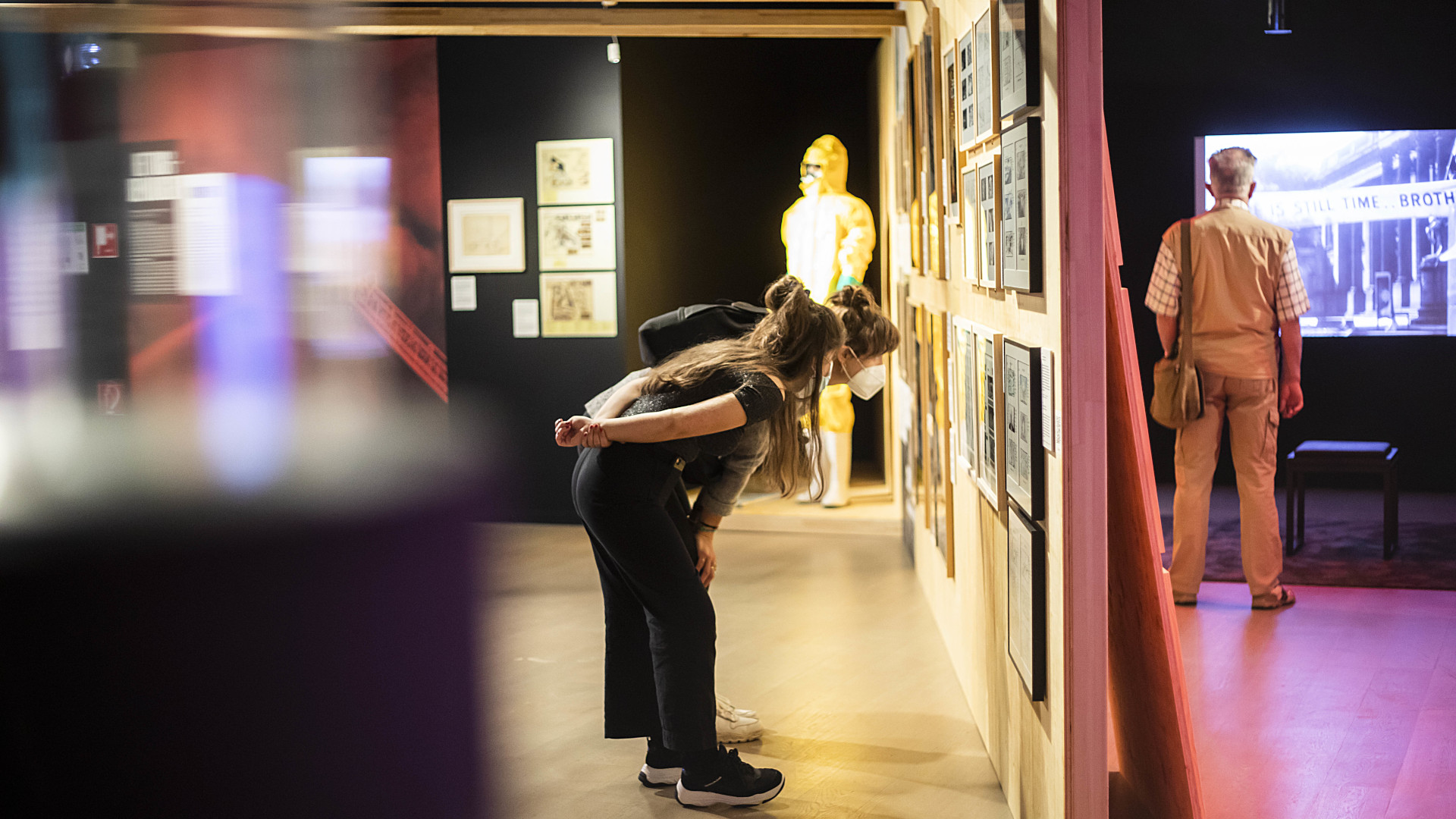 Zwei Ausstellungsbesucher:innen betrachten gerahmte Bilder an der Wand.