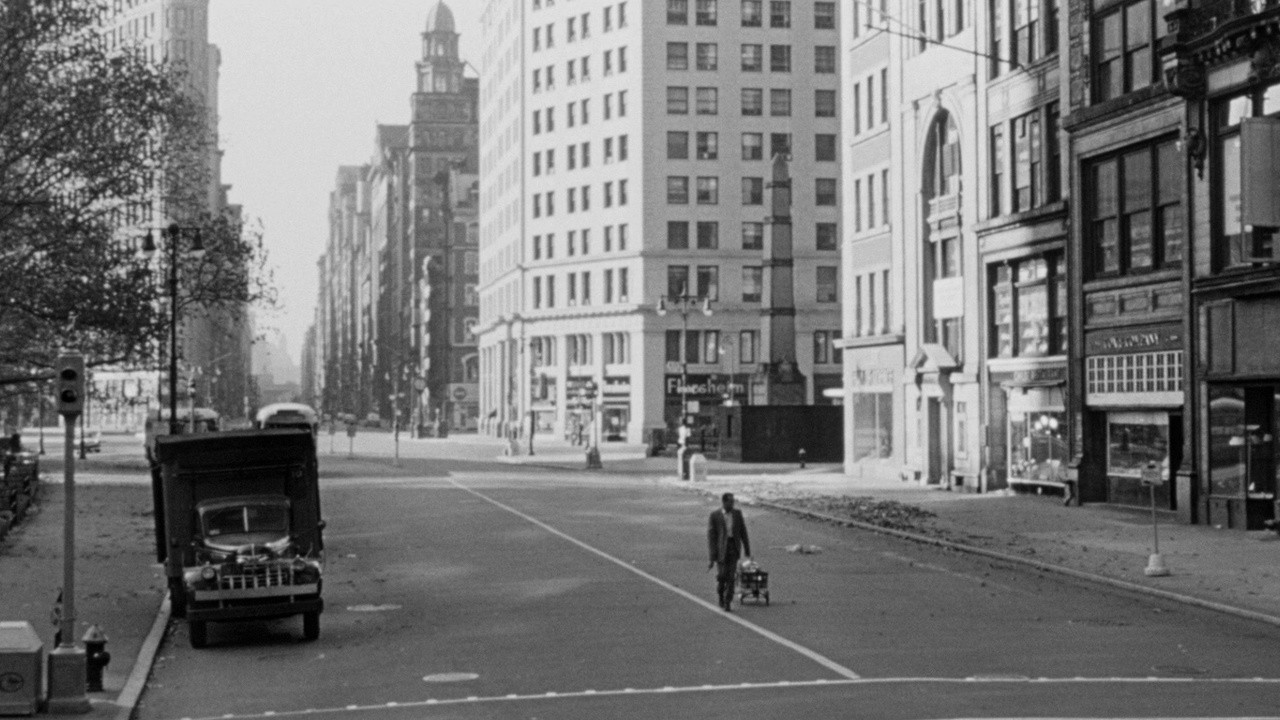 Filmstill aus dem Schwarz-Weiß-Film The World, the Flash and the Devil. Ein Mann geht eine breite Straße entlang. Am Straßenrand steht eine Lastwagen aus früherer Zeit und im Hintergrund stehen hohe Häuser.