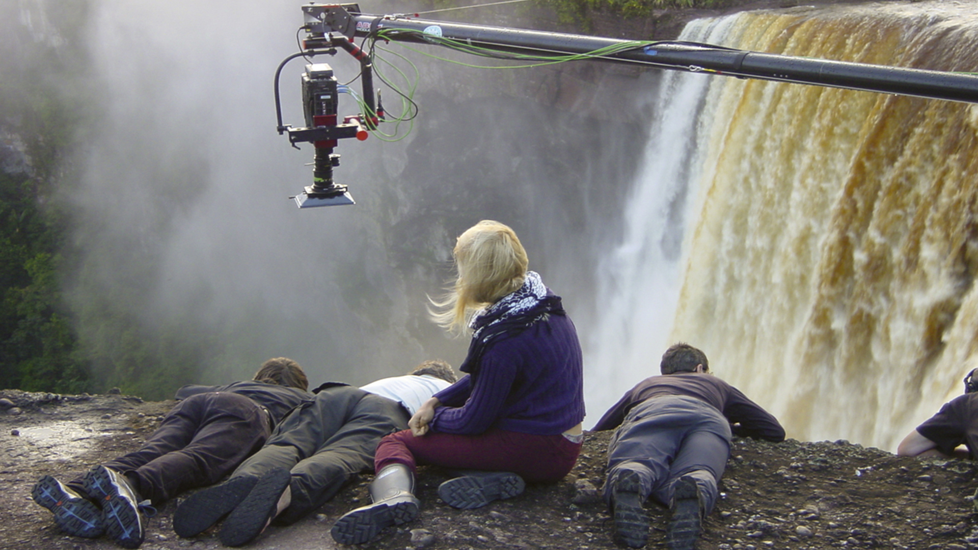 Hinter den Kulissen von dem Film The White Diamond. Vier Kinder sitzen und liegen an einem Abgrund zu einem Wasserfall hin. Darüber hängt eine Kamera herab.