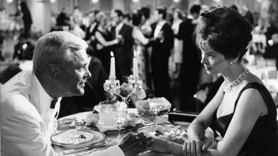 Filmstill aus Die Tausend Augen des Dr. Mabuse. Eine Frau und ein Mann sitzen an einem Tisch und im Hintergrund tanzen einige Paare.