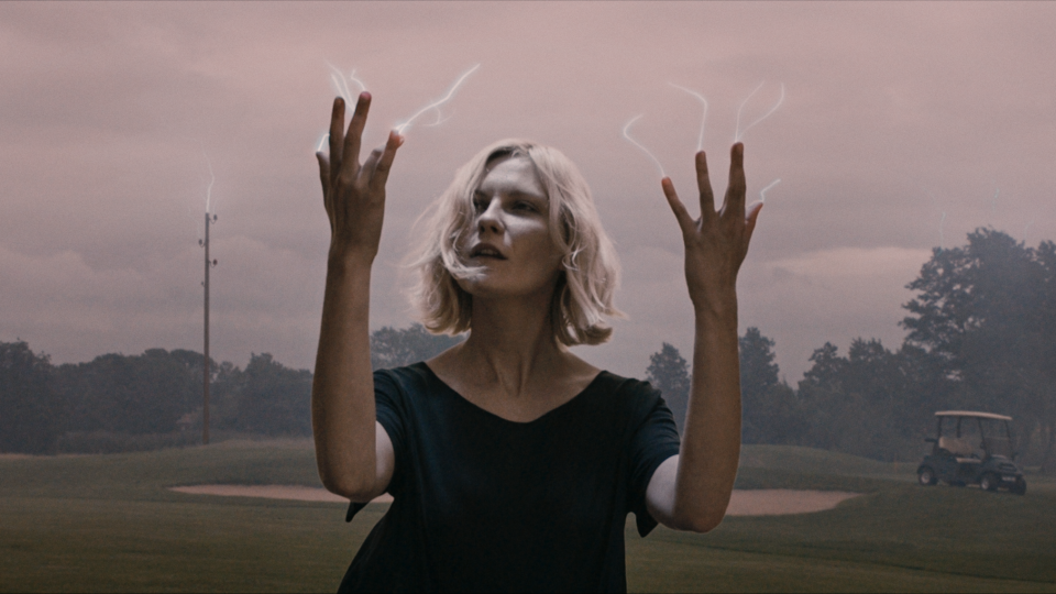 Filmstill aus Melancholia. Eine Frau hält ihre Hände in die Luft, aus deren Fingerspitzen weiße Fäden aufsteigen.