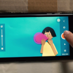 Smartphone zeigt Trickfilmbild mit Mädchen und einem rosa Ballon