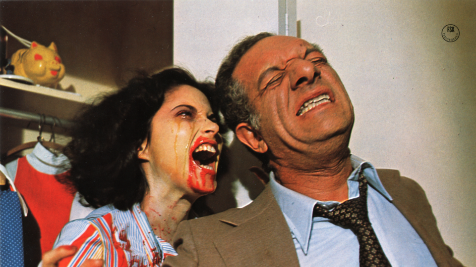 Filmstill aus dem Film Rabid. Eine Frau mit roter Farbe im Gesicht und weinend schreit einen Mann an, der mit dem Rücken zu ihr steht und ebenfalls das Gesicht verzieht.