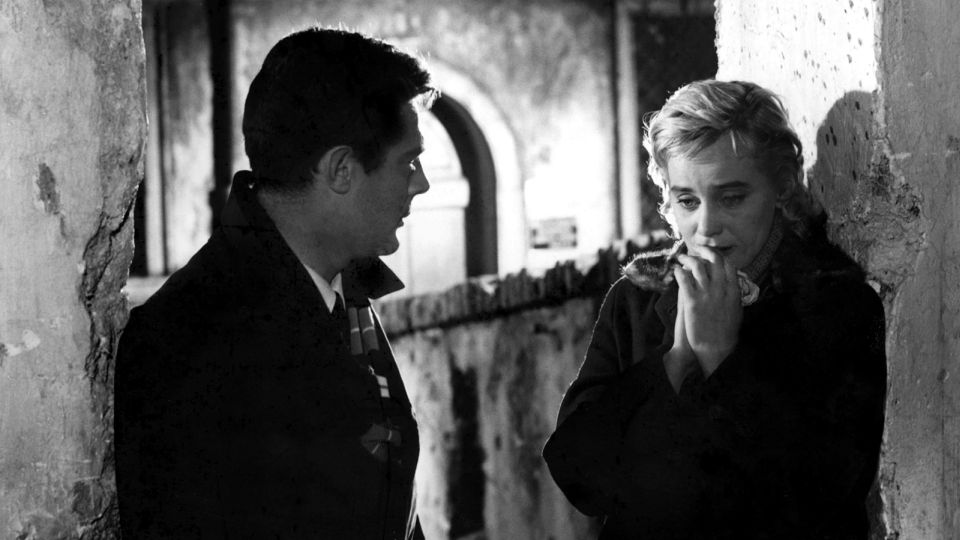 Filmstill aus dem Schwarz-Weiß-Film Le Notti Bianche. Ein Mann un eine Frau stehen zwischen zwei Säulen.
