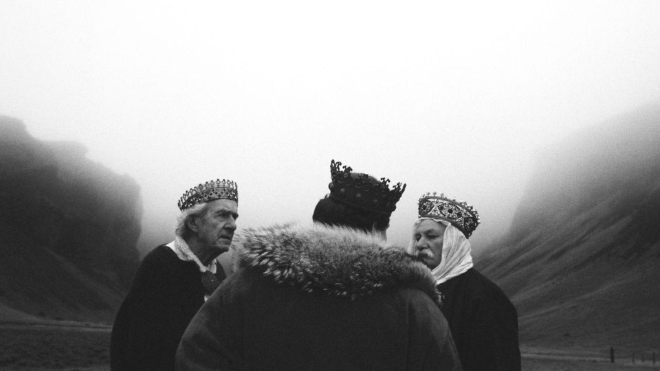 Filmstill aus El Kant del Ocells. Die schwarz weiß Aufnahme zeigt einen Mann mit Krone auf dem Kopf von hinten und zwei weitere Männer von vorne.