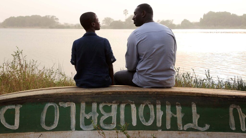 Filmstill YAO, Zwei Männliche Personen sitzen auf einem Boot an einem See mit dem Rücken zur Kamera