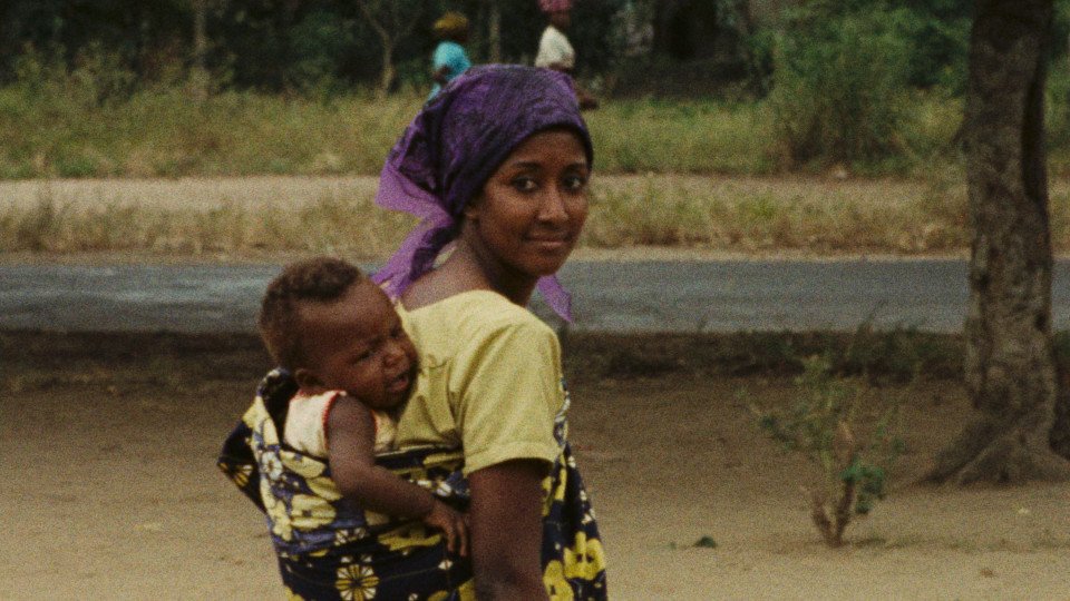 Filmstill aus Sambizanga: Eine Frau trägt einen Jungen iin einem Tragetuch auf dem Rücken und blickt über die rechte Schulter zurück