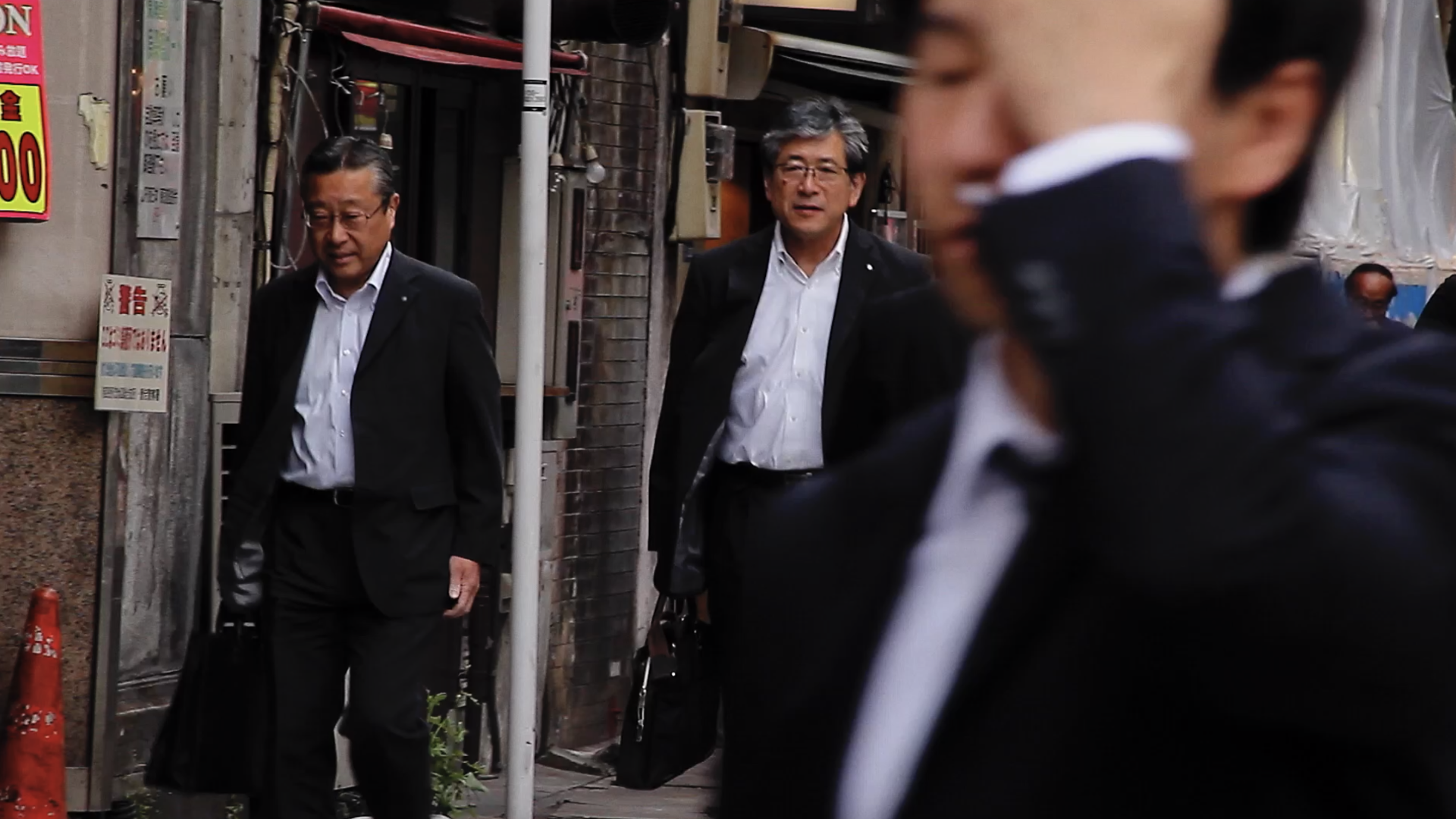 Filmstill aus Salaryman: Geschäftsleute in Anzügen und mit Aktentaschen laufen durch eine Straße.