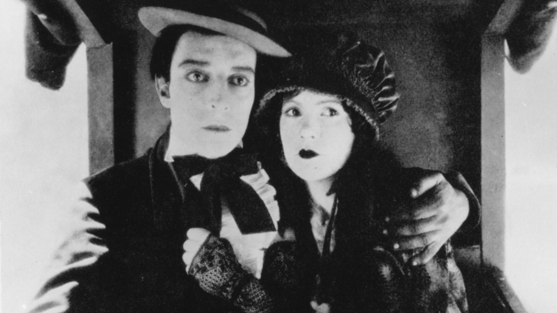 Filmstill aus Our Hospitality: Ein Mann mit Hut, Anzug und Fliege hält eine Frau, ebenfalls mit Hut, im Arm.