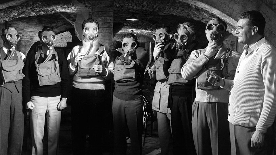 Filmstill aus The League of Gentlemen: Eine Gruppe Männer mit Atemschutzmasken in einem Keller