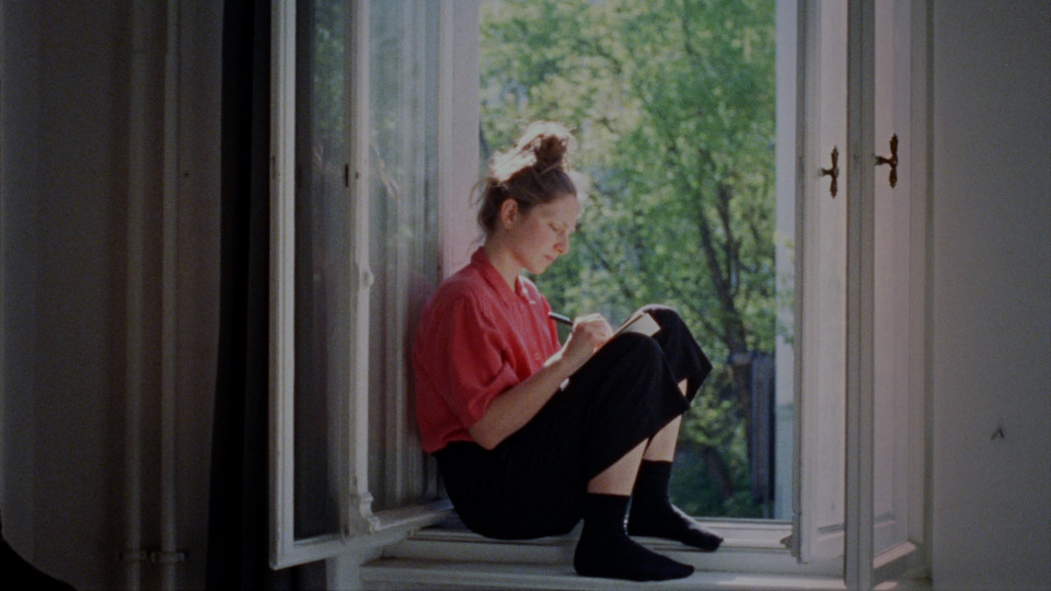 Filmstill aus Outside Noise: Eine Frau sitzt im Fensterrahmen udn schreibt in ein Heft