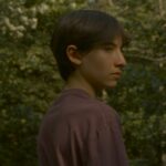 Filmstill aus FALCON LAKE: Der junge Hauptprotagonist des Films blickt verträumt in den Wald hinein.