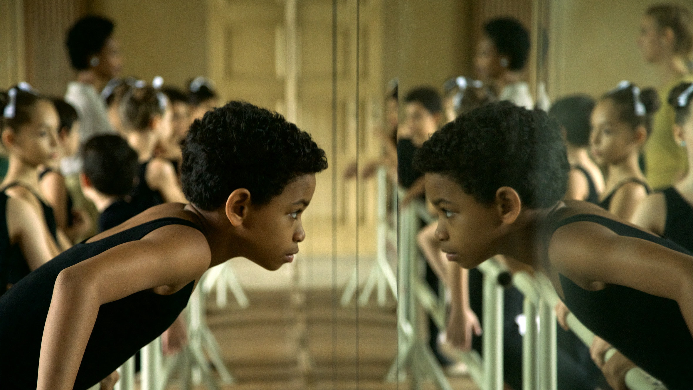 Ein Junge beugt sich über die Ballettstange und spiegelt sich an der Spiegelwand wieder.