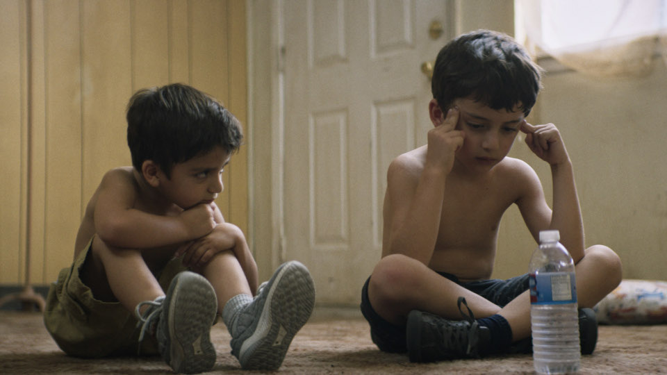 Filmstill aus Los Lobos: Zwei jungen mit nackten Oberkörpern sitzen auf dem Boden einer Wohnung