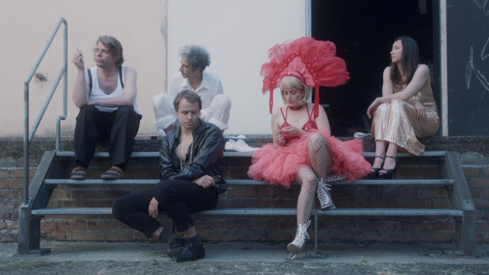 Filmstill aus Ladybitch: Fünf Personen sitzen auf einer Teppe, eine Frau trägt ein Show-Kostüm