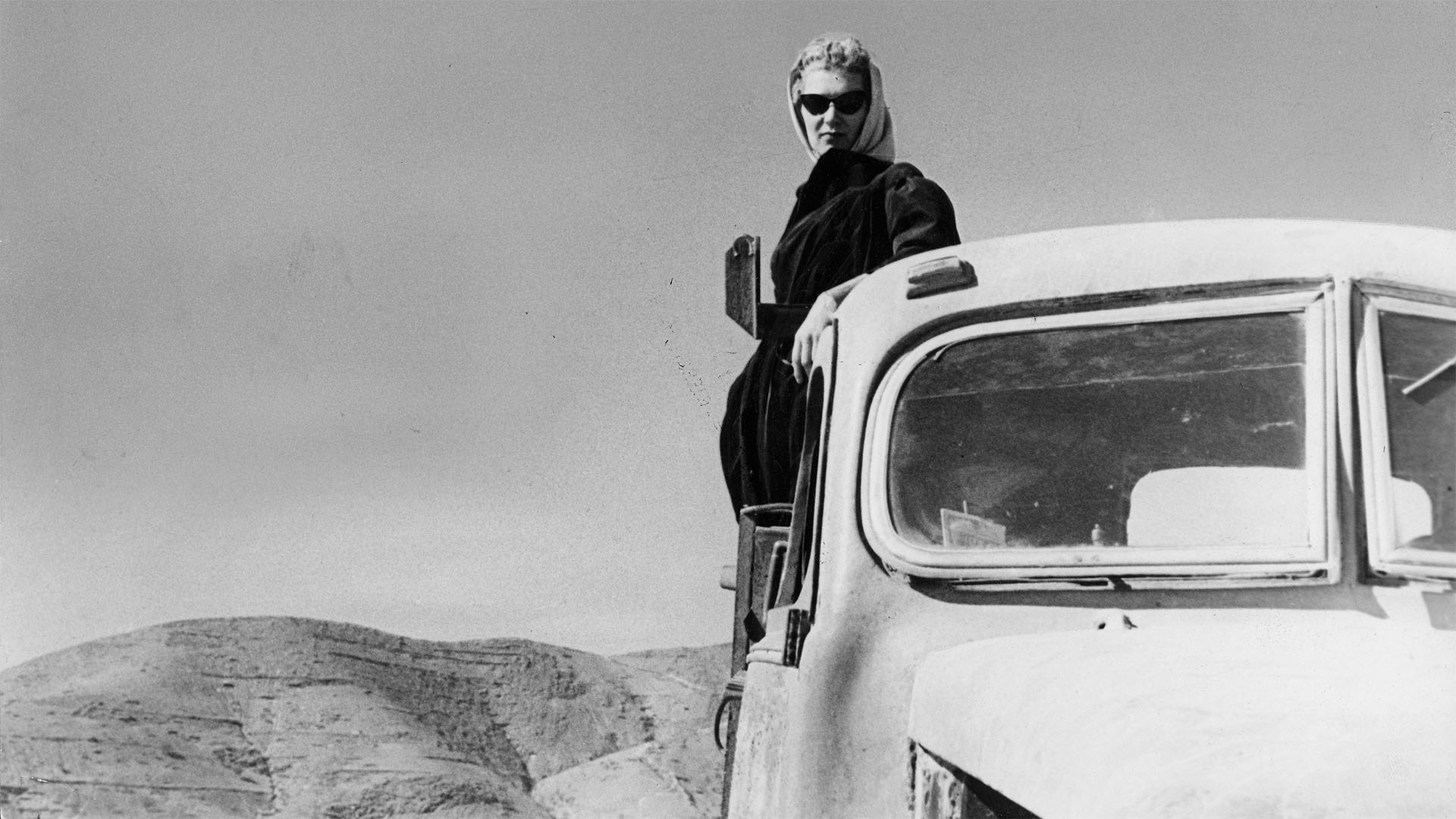 Frau 1950 er Jahre mit Kopftuch und Mantel auf der Ladefläche eines LKW in der Wüste