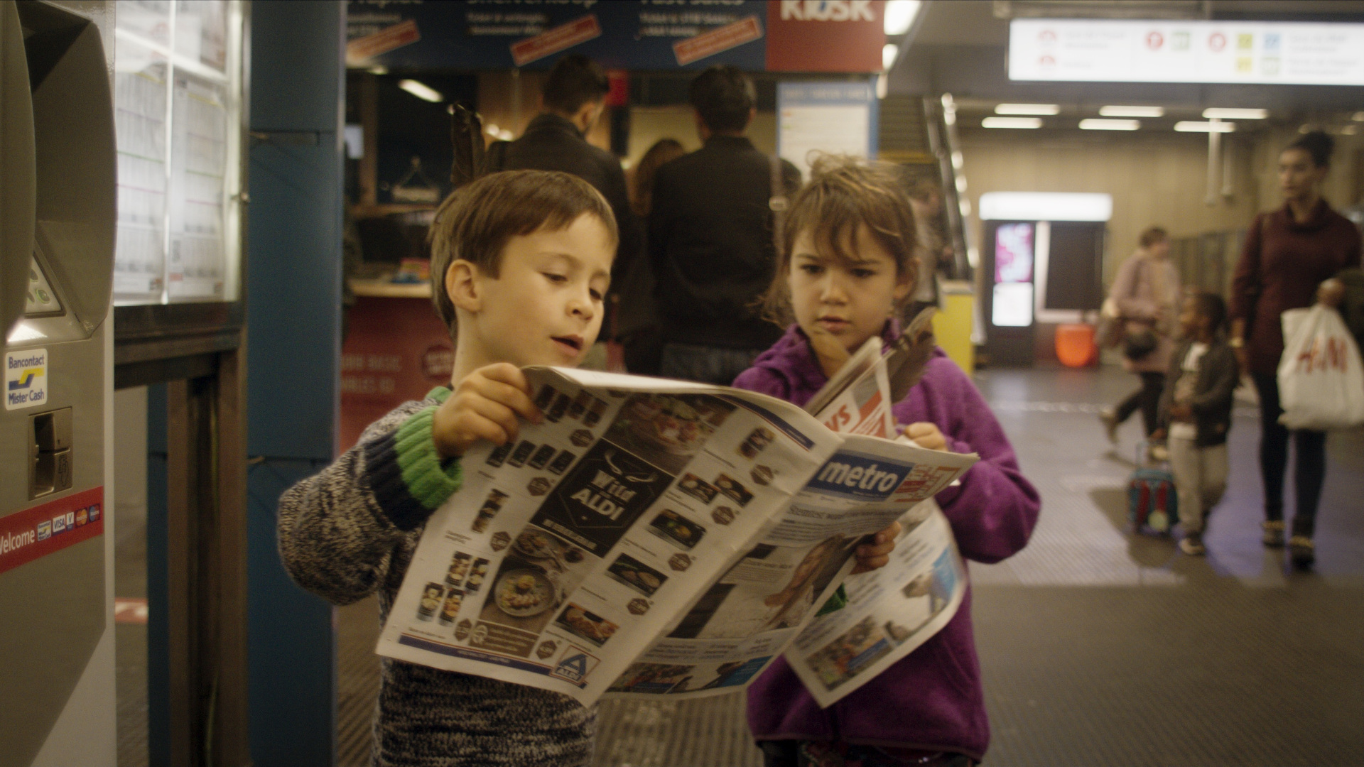 Filmstill aus Die Götter von Molenbeek: Zwei Kinder in einer Bahnstation lesen eine Zeitung